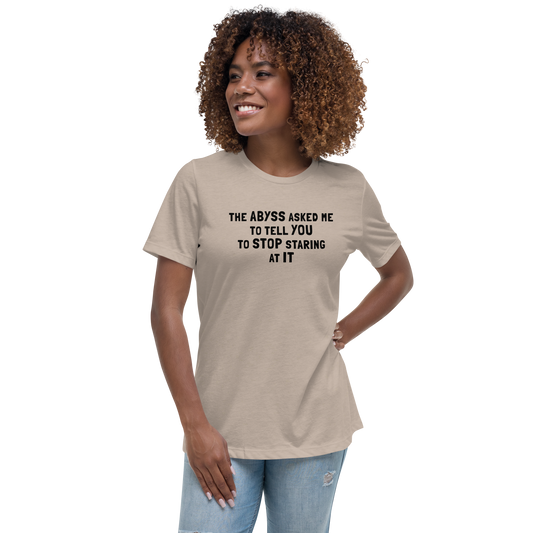 "The Abyss asked me to tell you to stop staring at it" printed on a heather stone women's relaxed t-shirt worn by a female