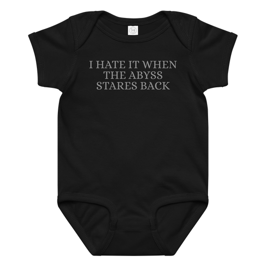 "I hate it when the abyss stares back" printed on a black baby jersey bodysuit laying on a flat surface amongst other clothes
