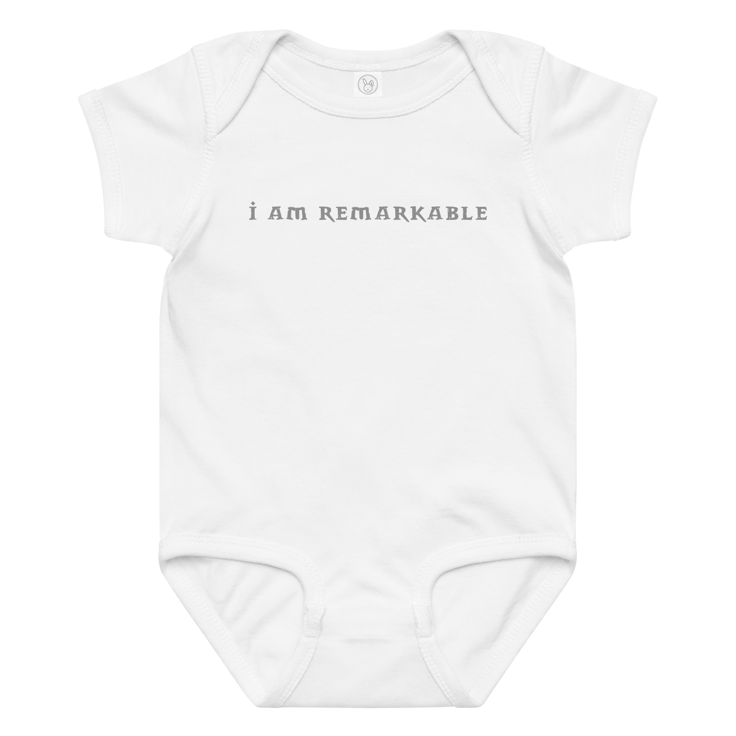 "I am remarkable" printed on a white baby jersey bodysuit laying on a flat surface amongst other clothes
