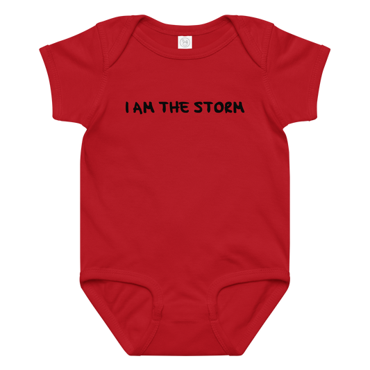 "I am the storm" printed on a red baby jersey bodysuit laying on a flat surface amongst other clothes