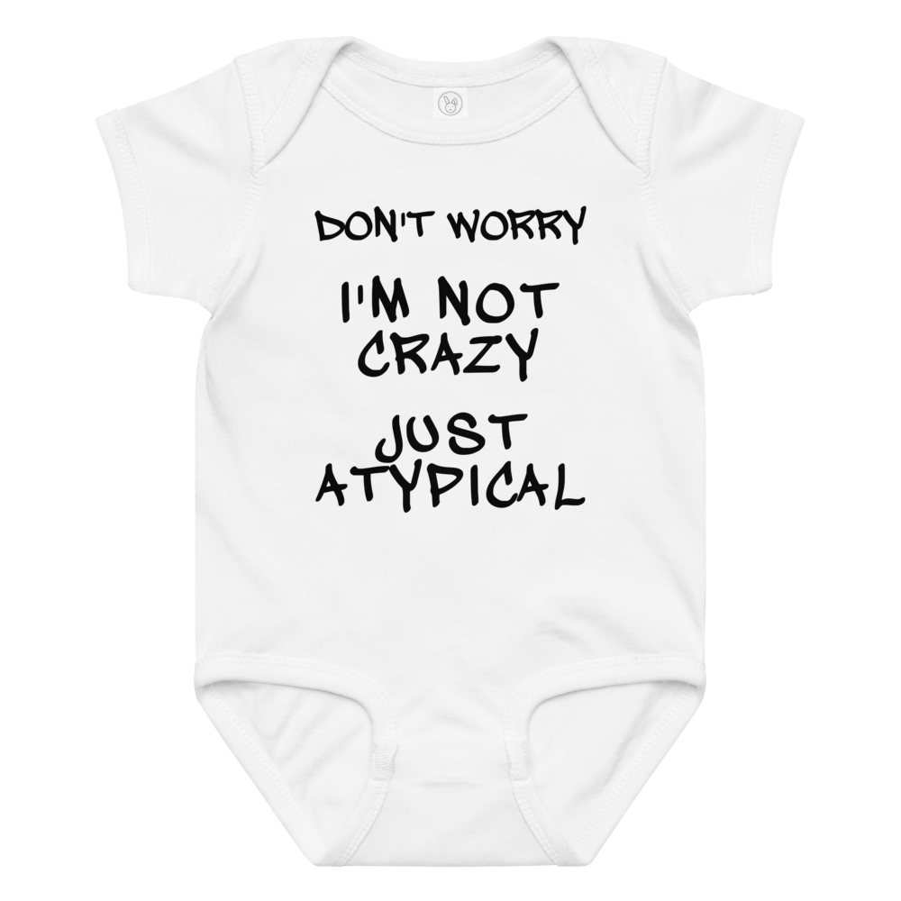 "Don't Worry I'm Not Crazy Just Atypical" printed on a white baby jersey bodysuit laying on a flat surface amongst other clothes