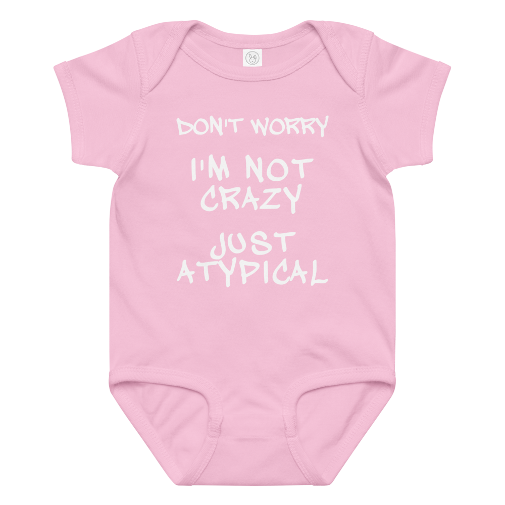 "Don't Worry I'm Not Crazy Just Atypical" printed on a pink baby jersey bodysuit laying on a flat surface amongst other clothes