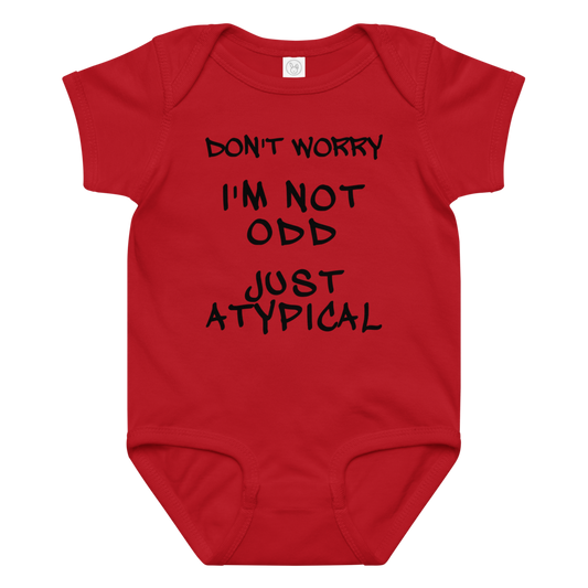 "Don't Worry I'm Not Odd Just Atypical" printed on a red baby jersey bodysuit laying on a flat surface amongst other clothes