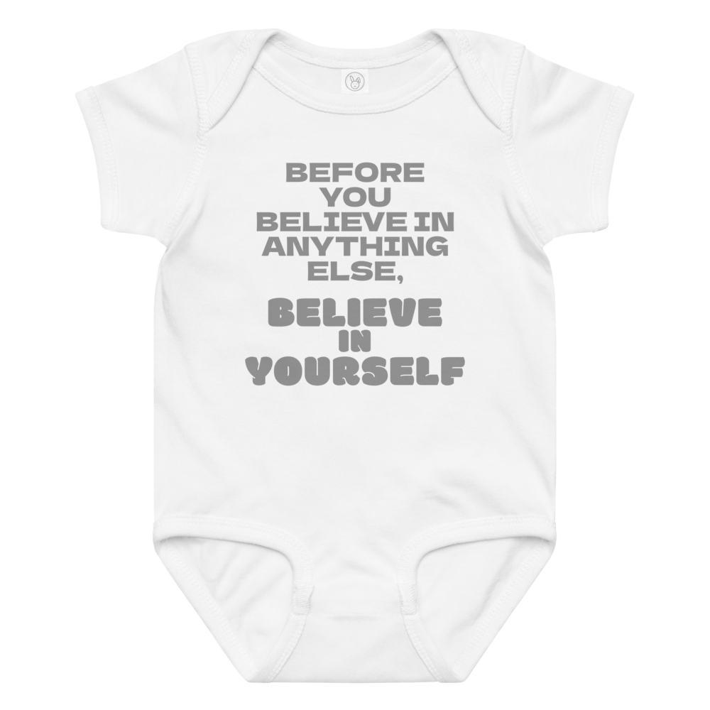 "Before you believe in anything else, believe in yourself" printed on a white baby jersey bodysuit laying on a flat surface amongst other clothes