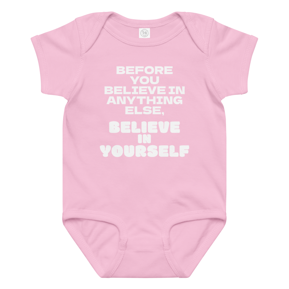 "Before you believe in anything else, believe in yourself" printed on a pink baby jersey bodysuit laying on a flat surface amongst other clothes