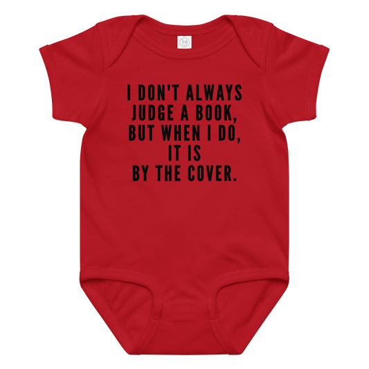 "I Don't always Judge a Book, but when I do, it's by the cover." printed on a red baby jersey bodysuit laying on a flat surface amongst other clothes