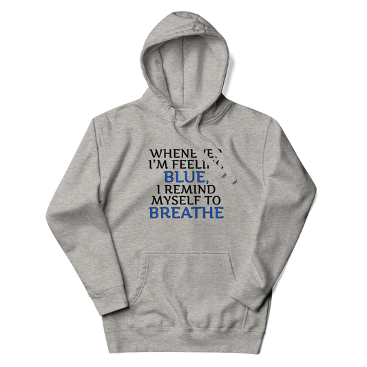 "Whenever I'm feeling blue, I remind myself to breathe" printed on a carbon grey unisex hoodie laying on a flat surface with the hood up