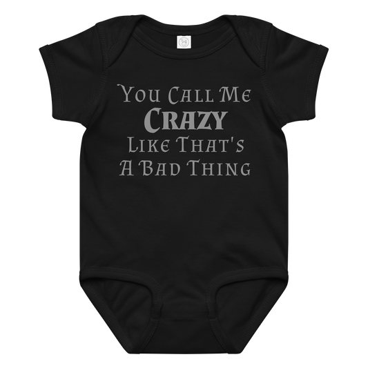 "You Call Me Crazy Like That's A Bad Thing" printed on a black baby jersey bodysuit laying on a flat surface amongst other clothes