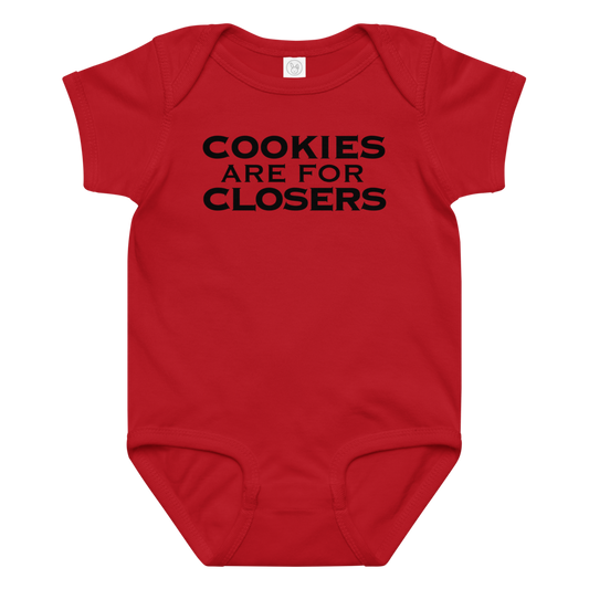 "Cookies Are For Closers" printed on a red baby jersey bodysuit laying on a flat surface amongst other clothes