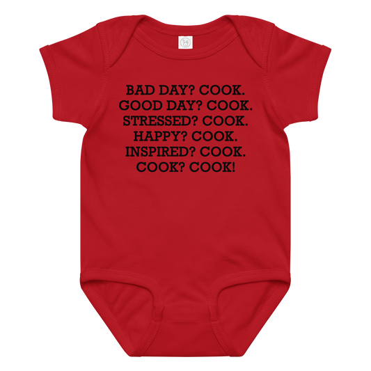 "Bad Day? Cook. Good Day? Cook. Stressed? Cook. Happy? Cook. Inspired? Cook. Cook? Cook!" printed on a red baby jersey bodysuit laying on a flat surface amongst other clothes