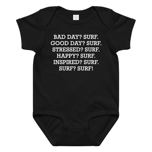 "Bad Day? Surf. Good Day? Surf. Stressed? Surf. Happy? Surf. Inspired? Surf. Surf? Surf!" printed on a black baby jersey bodysuit laying on a flat surface amongst other clothes