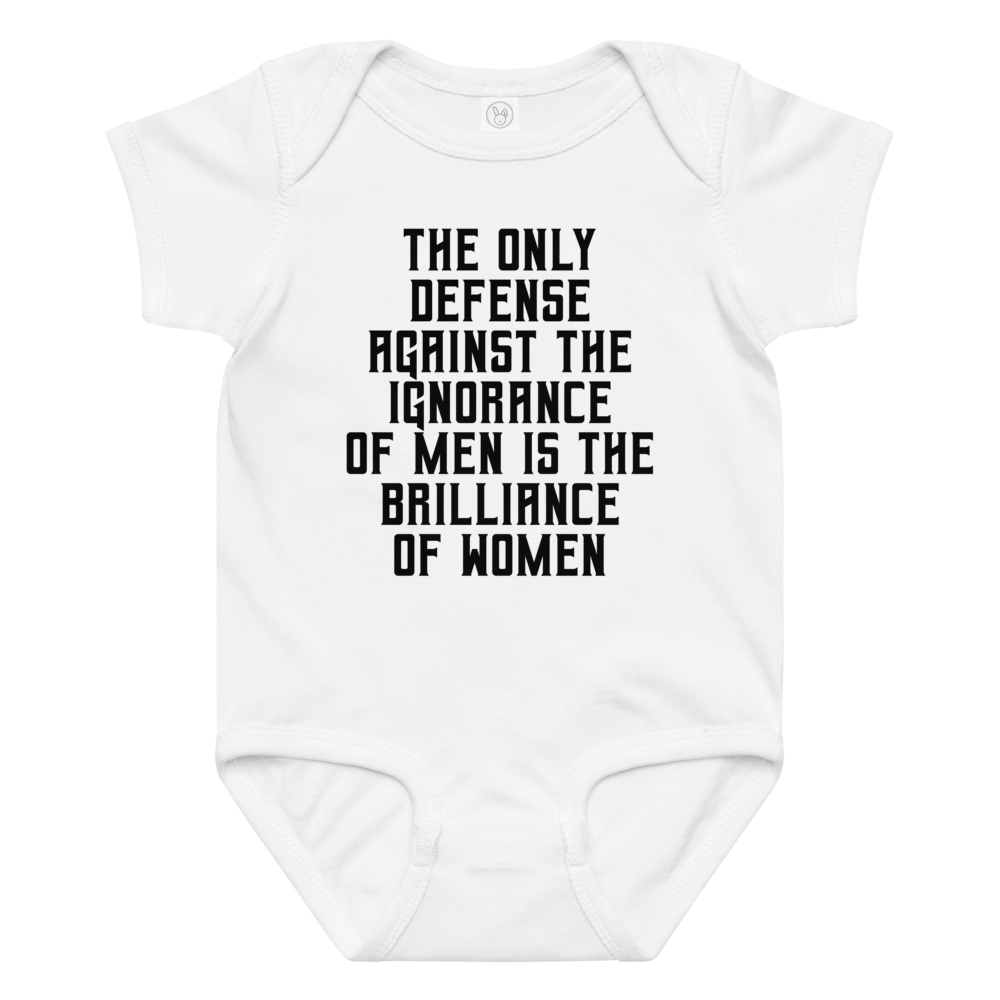 "The Only defense against the ignorance of men is the brilliance of women" printed on a white baby jersey bodysuit laying on a flat surface amongst other clothes