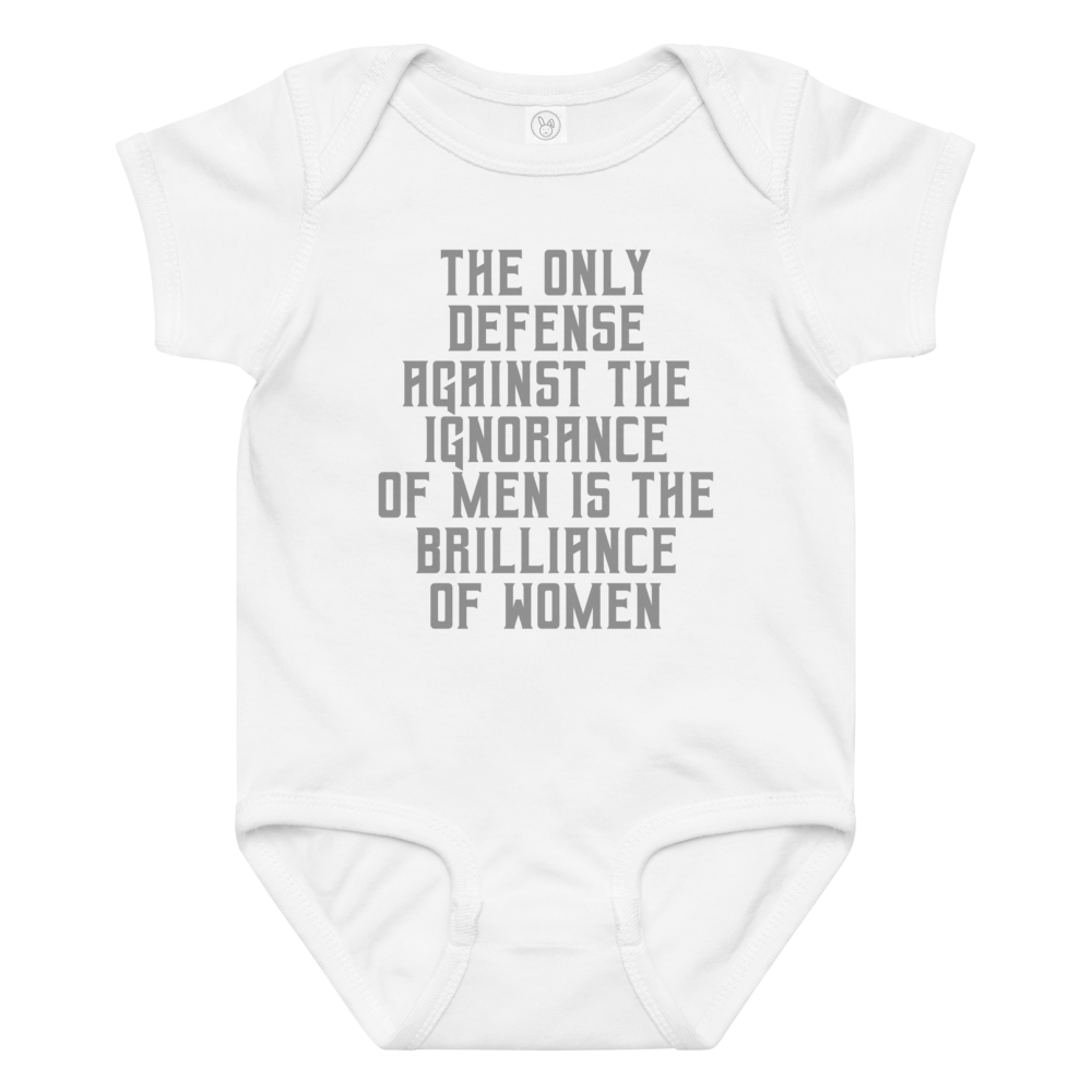 "The Only defense against the ignorance of men is the brilliance of women" printed on a white baby jersey bodysuit laying on a flat surface amongst other clothes