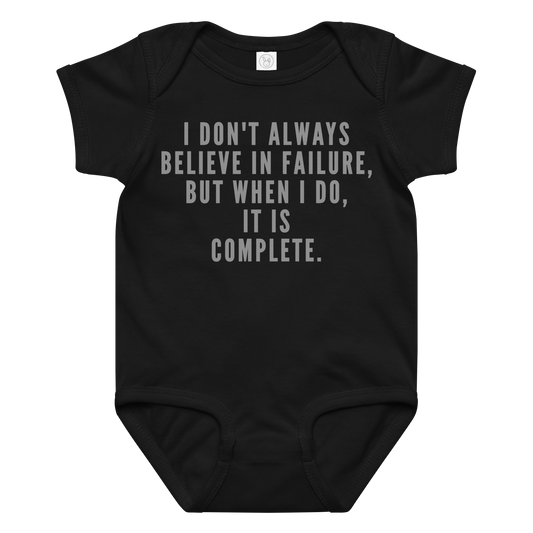 "I don't always believe in failure, but when I do, it is complete." printed on a black baby jersey bodysuit laying on a flat surface amongst other clothes