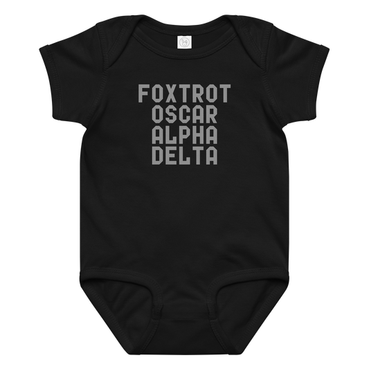 "Foxtrot Oscar Alpha Delta" printed on a black baby jersey bodysuit laying on a flat surface amongst other clothes