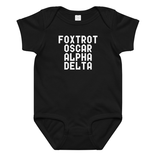 "Foxtrot Oscar Alpha Delta" printed on a black baby jersey bodysuit laying on a flat surface amongst other clothes