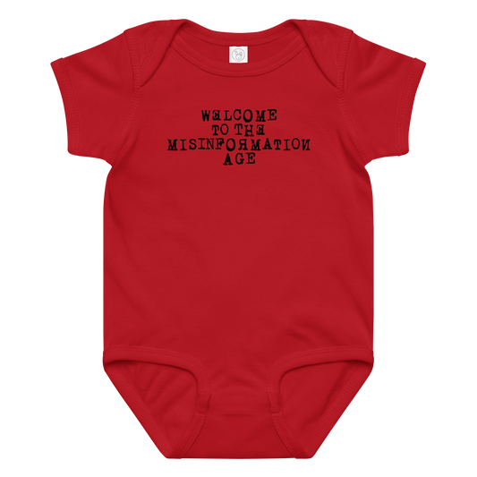 "Welcome to the misinformation age" printed on a red baby jersey bodysuit laying on a flat surface amongst other clothes
