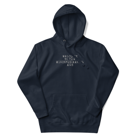 "Welcome to the misinformation age" printed on a navy blazer unisex hoodie laying on a flat surface with the hood up