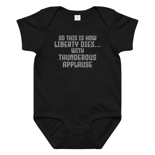 "So this is how liberty dies… with thunderous applause" printed on a black baby jersey bodysuit laying on a flat surface amongst other clothes