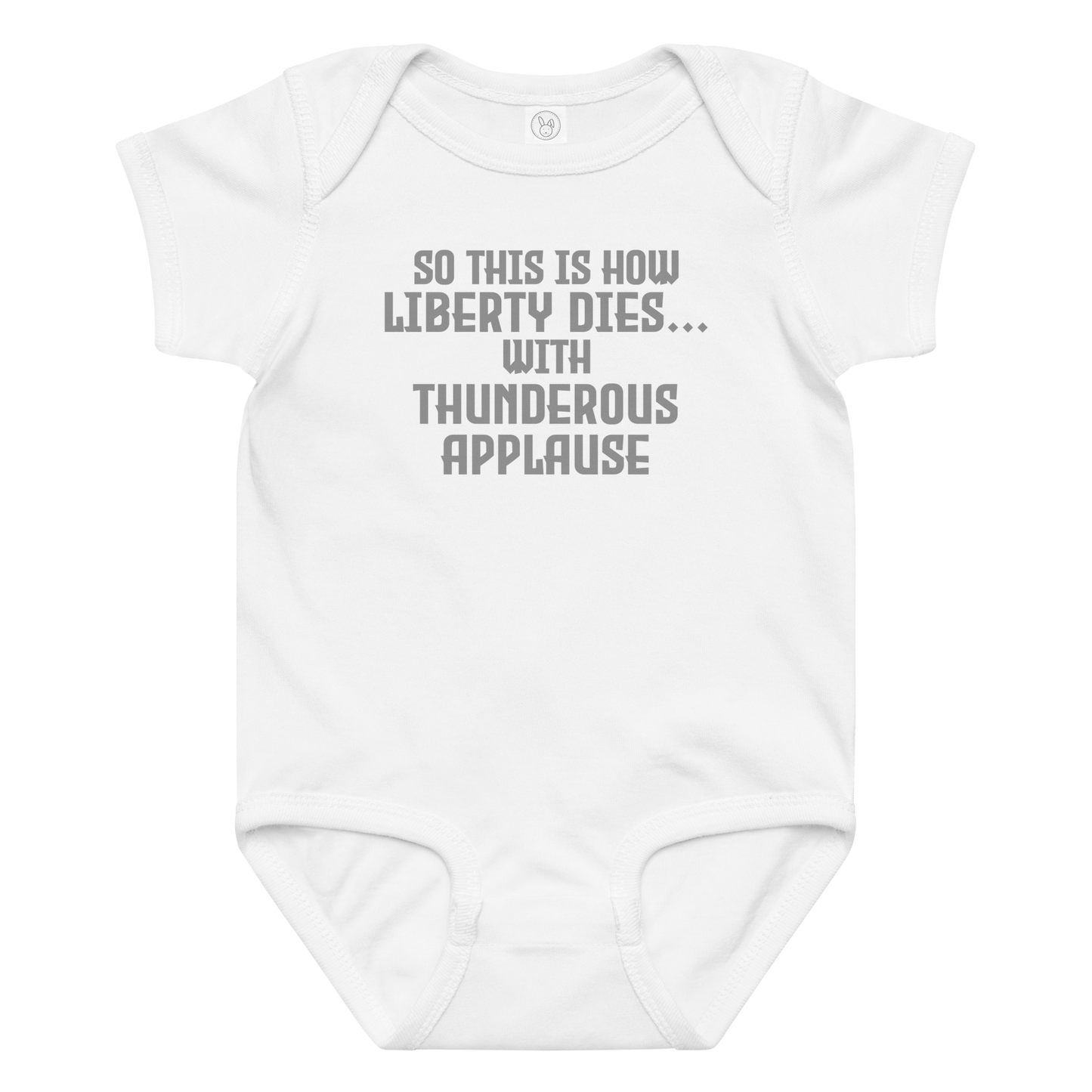 "So this is how liberty dies… with thunderous applause" printed on a white baby jersey bodysuit laying on a flat surface amongst other clothes