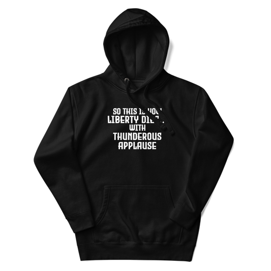 "So this is how liberty dies… with thunderous applause" printed on a black unisex hoodie laying on a flat surface with the hood up