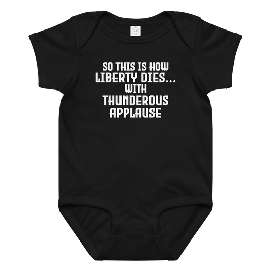 "So this is how liberty dies… with thunderous applause" printed on a black baby jersey bodysuit laying on a flat surface amongst other clothes
