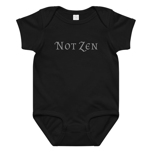 "Not zen" printed on a black baby jersey bodysuit laying on a flat surface amongst other clothes