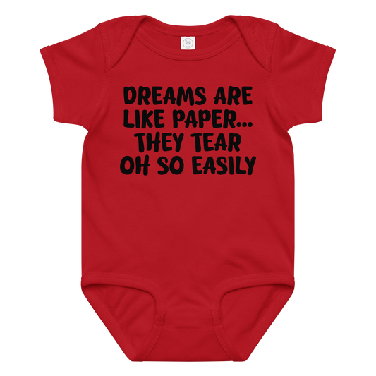 "Dreams are like paper, they tear oh so easily" printed on a red baby jersey bodysuit laying on a flat surface amongst other clothes
