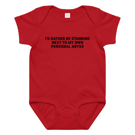 "I'd rather be standing next to my own personal abyss" printed on a red baby jersey bodysuit laying on a flat surface amongst other clothes