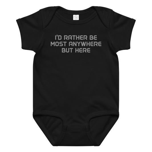 "I’d rather be most anywhere but here" printed on a black baby jersey bodysuit laying on a flat surface amongst other clothes