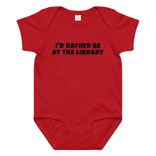 "I’d rather be at the library" printed on a red baby jersey bodysuit laying on a flat surface amongst other clothes