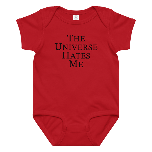 "The Universe Hates Me" printed on a red baby jersey bodysuit laying on a flat surface amongst other clothes