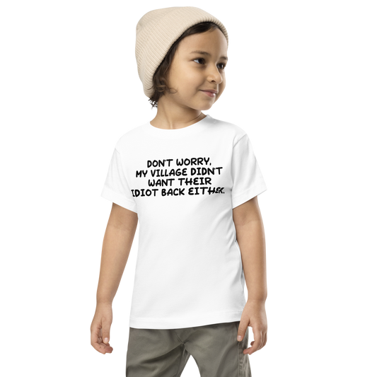 "Don't worry, my village didn’t want their idiot back either." printed on a white toddler short sleeve tee worn by a male wearing a cap