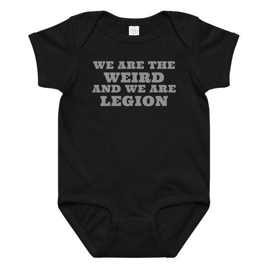 "We are the weird and we are legion" printed on a black baby jersey bodysuit laying on a flat surface amongst other clothes