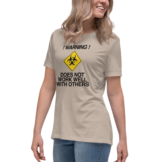 "!Warning! Does Not Work Well With Others" printed on a heather stone women's relaxed t-shirt worn by a female