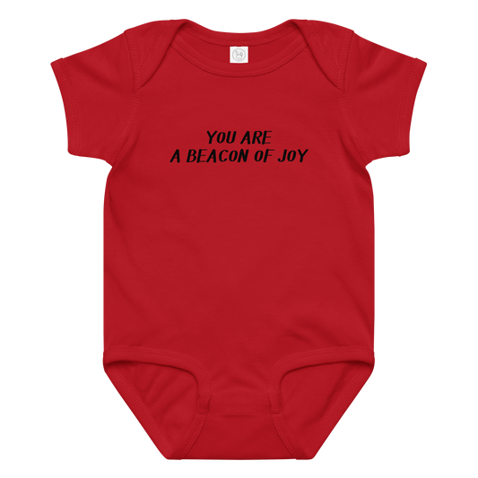 "You are a beacon of joy" printed on a red baby jersey bodysuit laying on a flat surface amongst other clothes