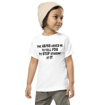 "The Abyss asked me to tell you to stop staring at it" printed on a white toddler short sleeve tee worn by a male wearing a cap