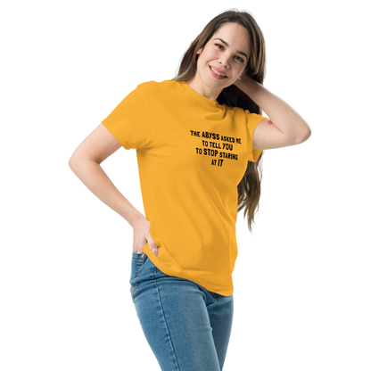 "The Abyss asked me to tell you to stop staring at it" printed on a gold unisex classic tee worn by a female