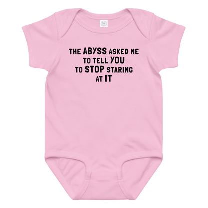 "The Abyss asked me to tell you to stop staring at it" printed on a pink baby jersey bodysuit laying on a flat surface amongst other clothes