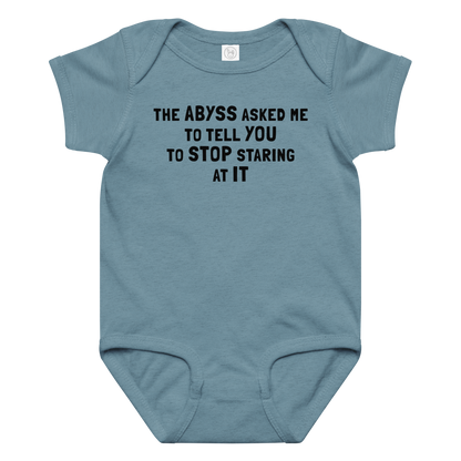 "The Abyss asked me to tell you to stop staring at it" printed on a vintage indigo baby jersey bodysuit laying on a flat surface amongst other clothes
