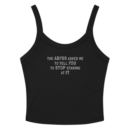 "The Abyss asked me to tell you to stop staring at it" printed on a solid black blend women's micro-rib tanktop laying on a flat surface amongst sunglasses and shorts