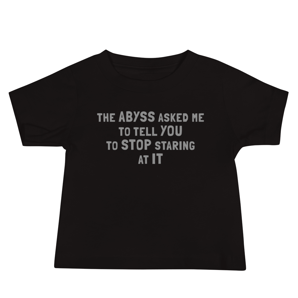 "The Abyss asked me to tell you to stop staring at it" printed on a black baby jersey short sleeve tee laying on a flat surface