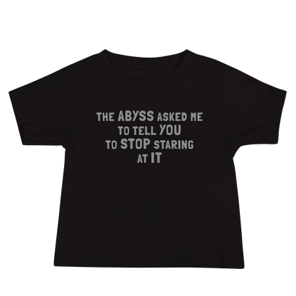 "The Abyss asked me to tell you to stop staring at it" printed on a black baby jersey short sleeve tee laying on a flat surface