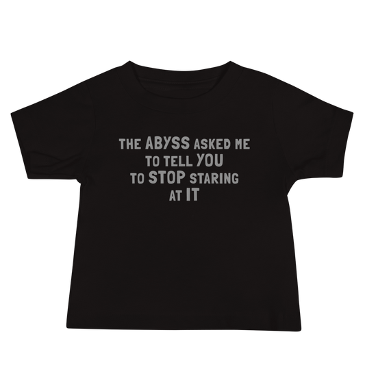 "The Abyss asked me to tell you to stop staring at it" printed on a black baby jersey short sleeve tee laying on a flat surface