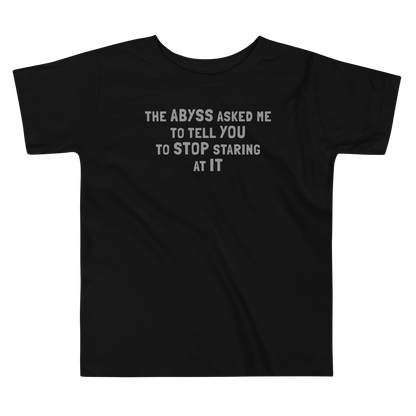 "The Abyss asked me to tell you to stop staring at it" printed on a black toddler short sleeve tee laying on a flat surface