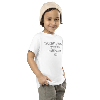 "The Abyss asked me to tell you to stop staring at it" printed on a white toddler short sleeve tee worn by a male who is also wearing a knit cap