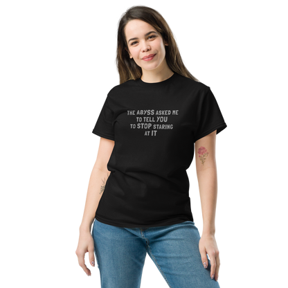 "The Abyss asked me to tell you to stop staring at it" printed on a black unisex classic tee worn by a female