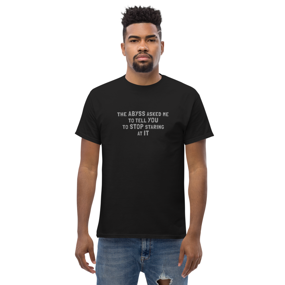 "The Abyss asked me to tell you to stop staring at it" printed on a black unisex classic tee worn by a male