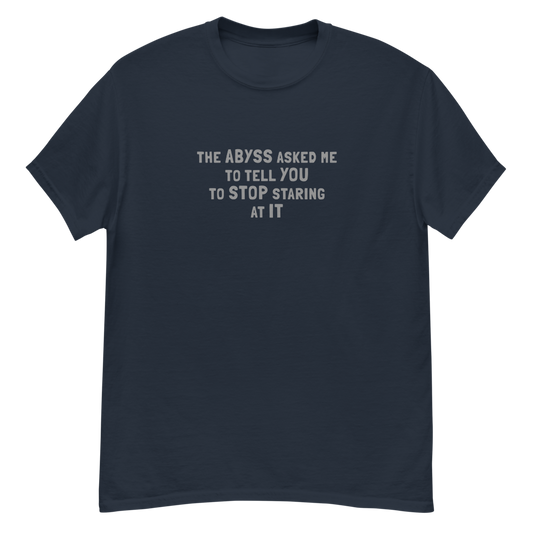 "The Abyss asked me to tell you to stop staring at it" printed on a navy unisex classic tee laying on a flat surface