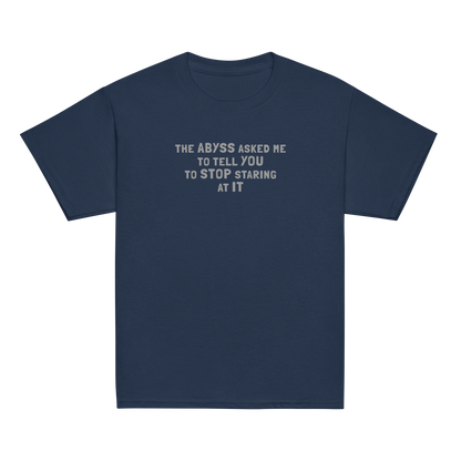 "The Abyss asked me to tell you to stop staring at it" printed on a navy youth classic tee laying on a flat surface